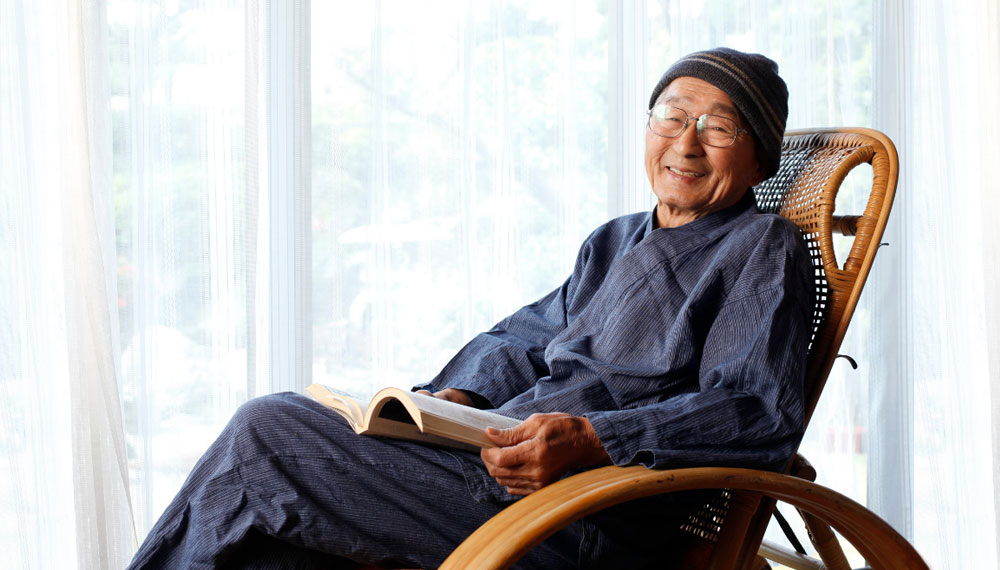 Senior man sitting in cane chair reading a book