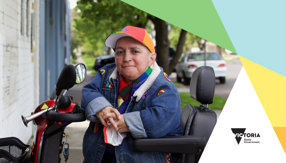 Person wearing a rainbow coloured cap sitting on mobility device