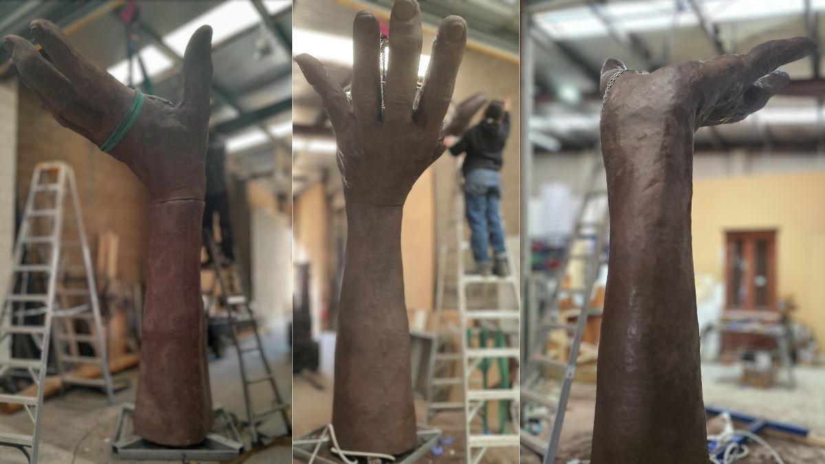 The artisans use ladders to put the final touches on the raised hand part of the scuplture.
