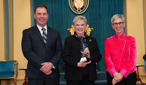 Premier’s Award for Victorian Senior of the Year 2022 awardee Moira Waye standing between Minister Chris Brooks and Governor of Victoria Linda Dessau. They are all smiling at the camera.