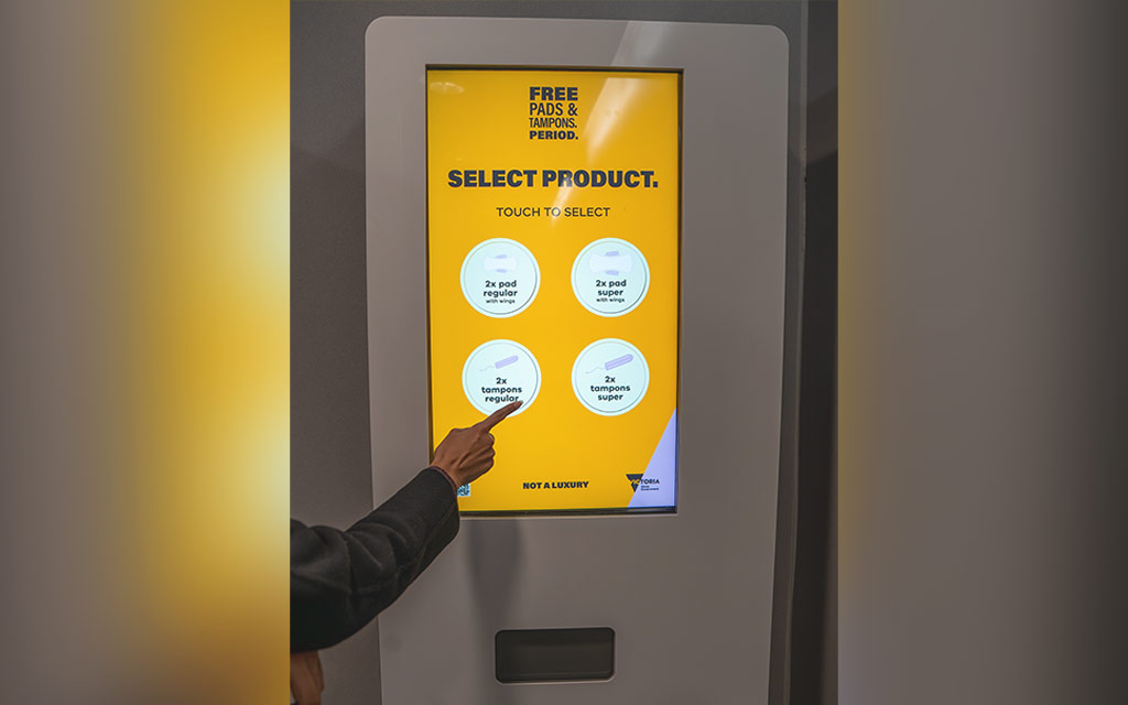 A person selecting a product from a touchscreen pads and tampons vending machine
