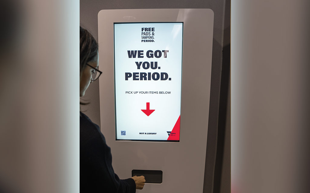 A person collecting a product from a touchscreen pads and tampons vending machine