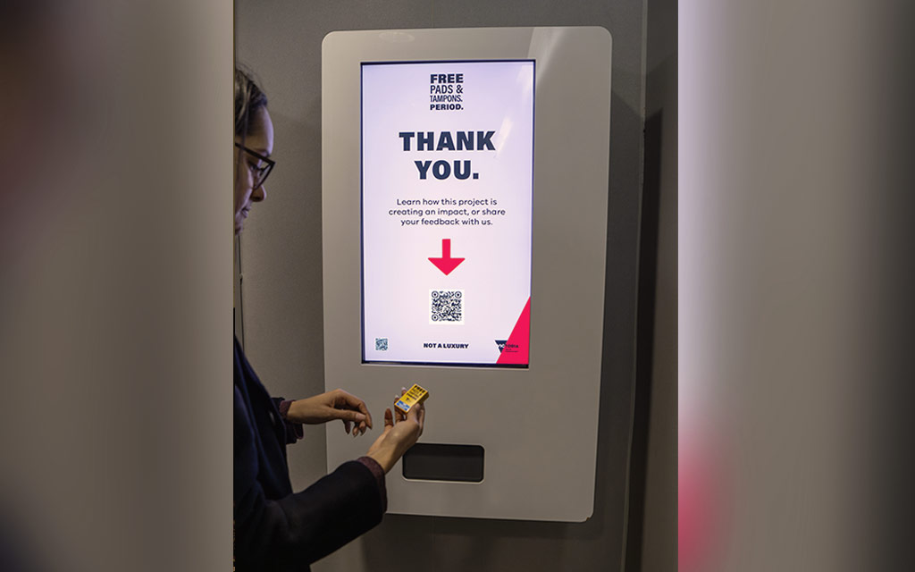 A person holding a product from a touchscreen pads and tampons vending machine