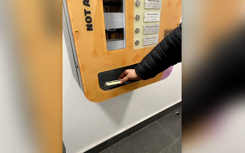 A person collecting a product from a pads and tampons vending machine