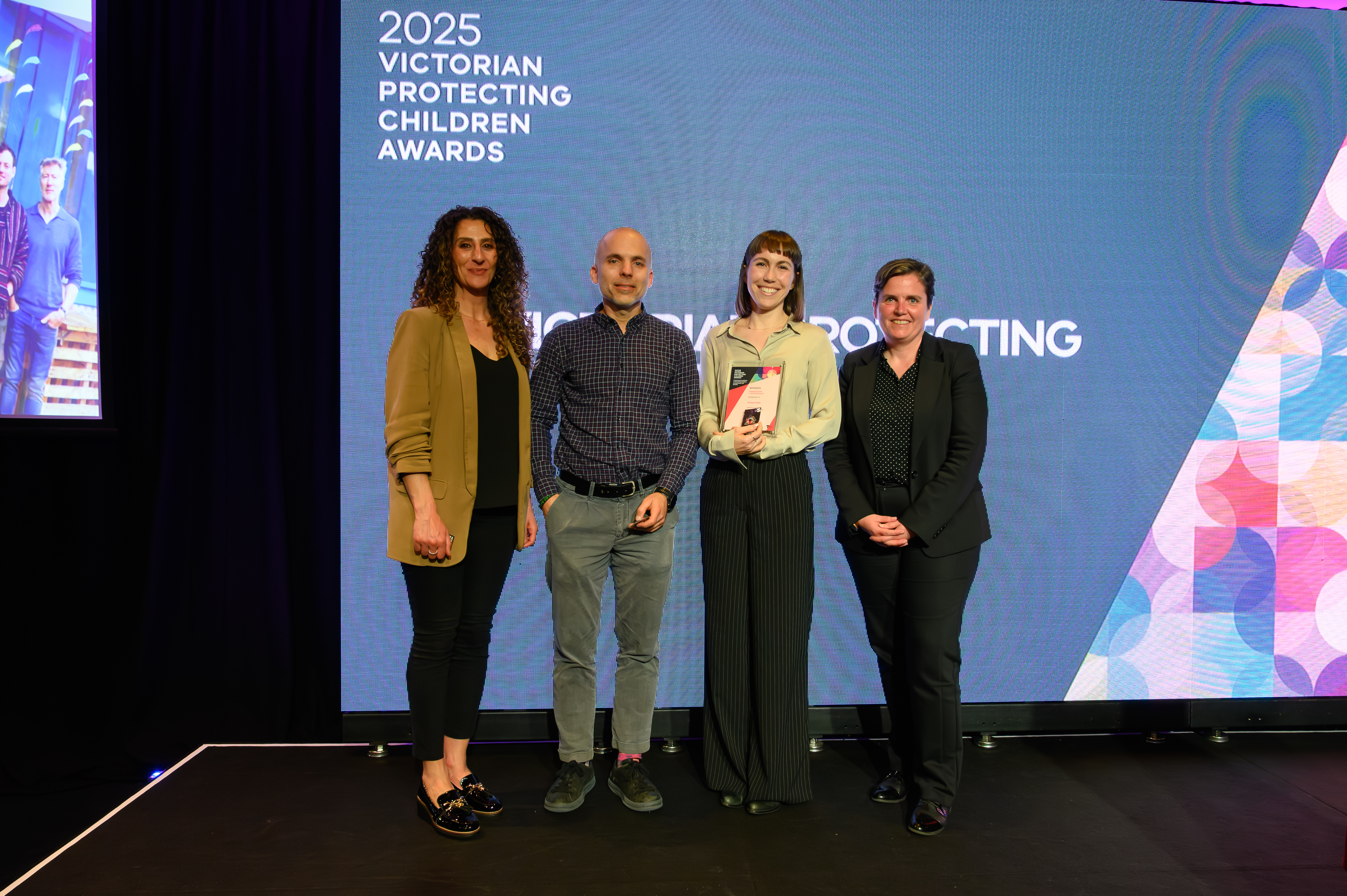 Four people standing on the stage of an award show; one person is holding an award.