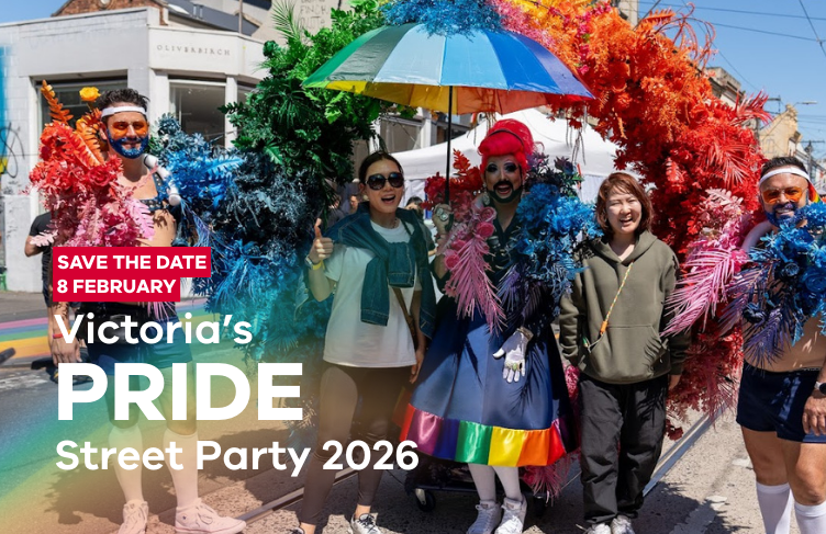 A drag queen surrounded by women and male marching band under a rainbow coloured feather arch. arch
