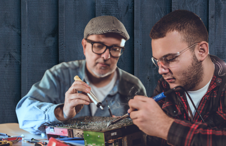 Two men using soldering irons on a circuit board.