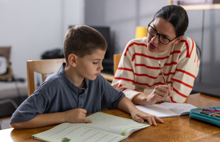 Child and adult sitting at a table. The child is doing homework.